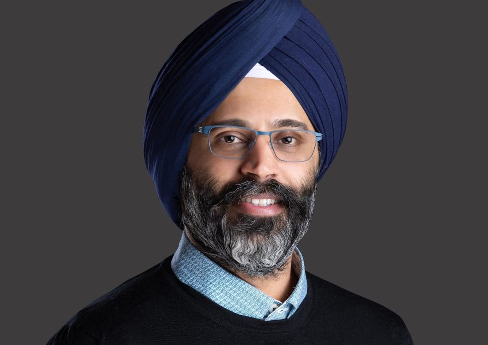 Karandeep Anand with glasses and turban smiling, wearing a black sweater against a gray background.