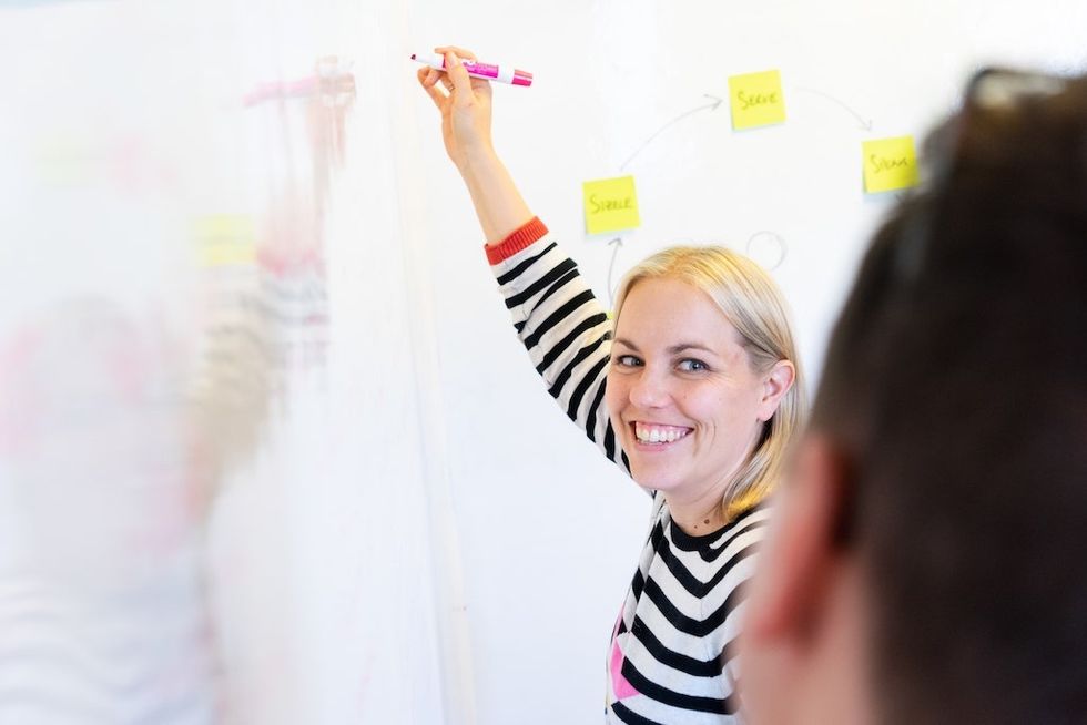 Katapult's Dawn foote smiling, writing on a whiteboard with sticky notes and diagrams.