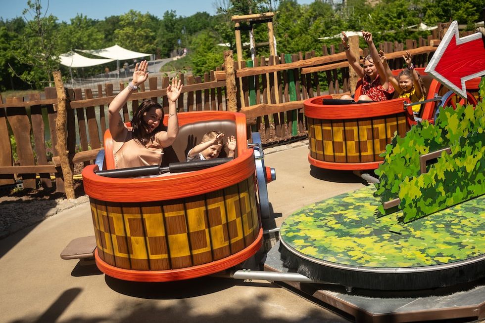 Kids and adults enjoy an amusement ride in spinning barrel seats on a sunny day.
