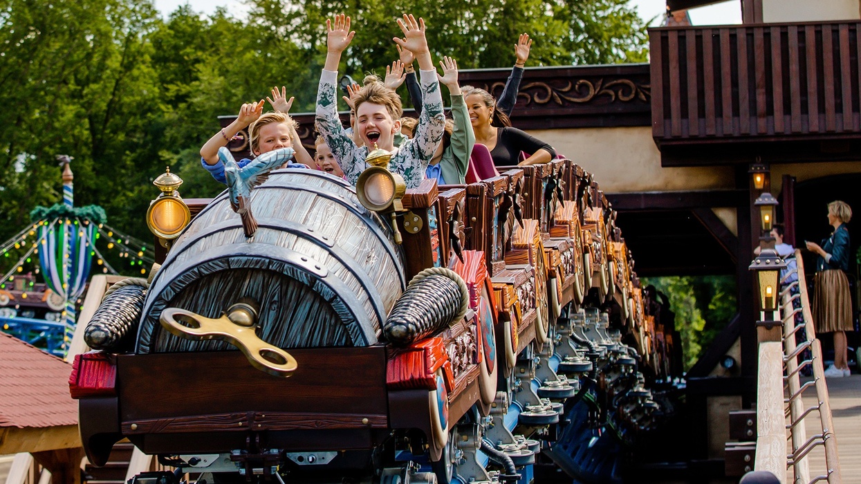 Kids enjoying a roller coaster ride with hands raised, surrounded by trees.