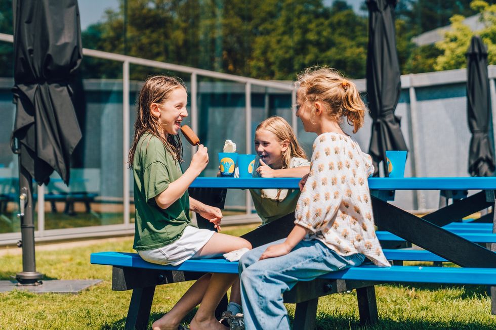 Kids enjoying ice cream and drinks at a blue picnic table on a sunny day.