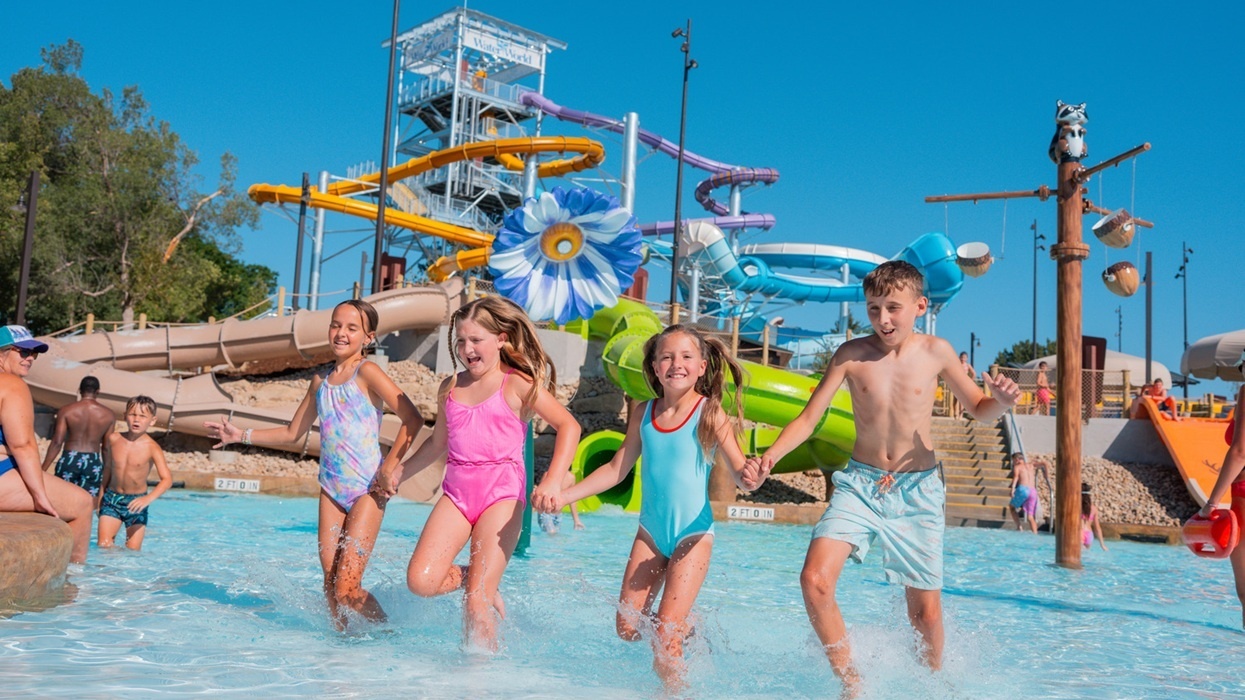 Kids joyfully splash in a pool at Summit Canyon at Water World in Colorado ,with colourful slides in the background.