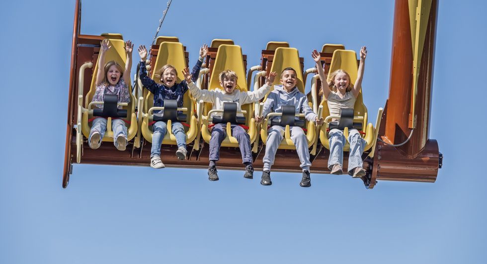 Kids on a thrill ride with arms raised, against a clear blue sky.