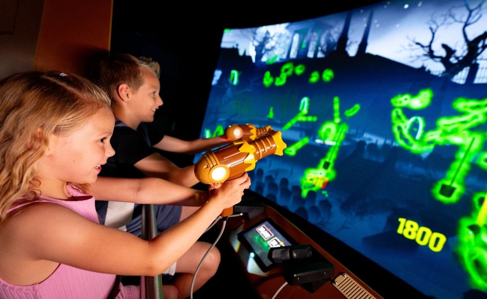 Kids playing an interactive arcade shooting game with neon graphics.