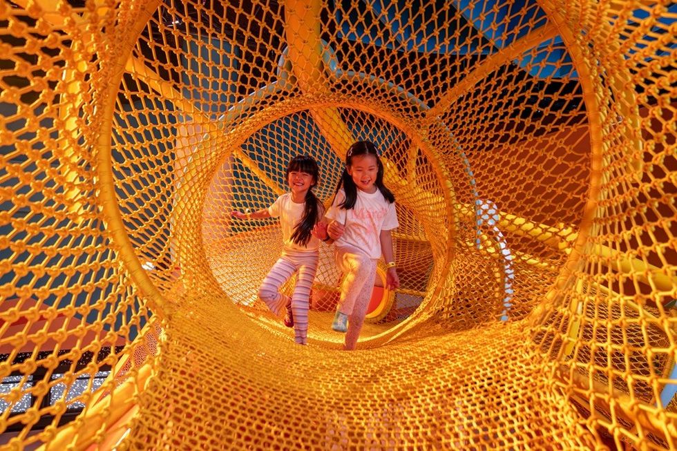 Kids playing in a bright yellow netted tunnel.
