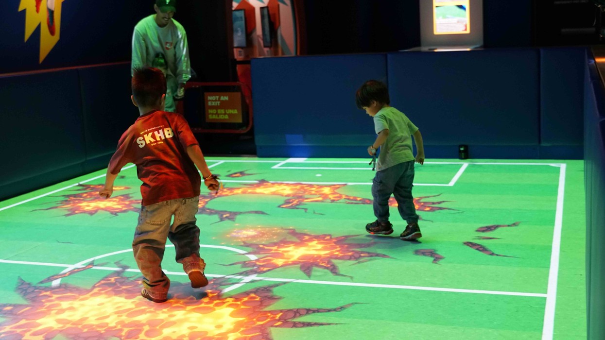 Kids playing on interactive projection floor with lava cracks in a dark room.
