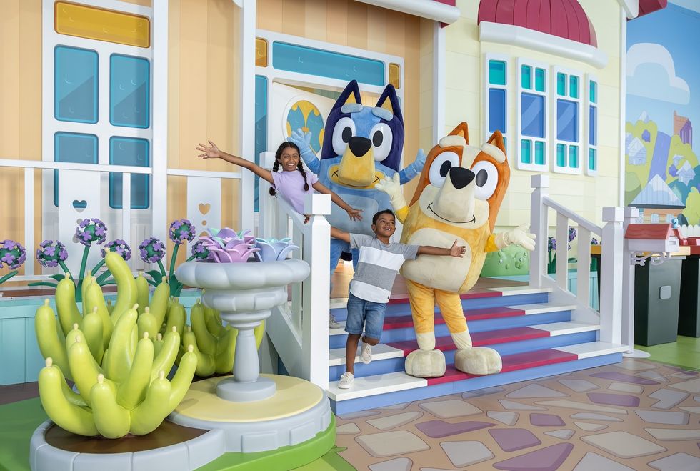 Kids posing with Bluey and Bingo characters in front of a colorful house backdrop.