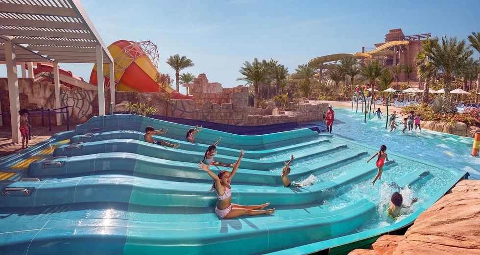 Kids sliding down water slides at a tropical water park with palm trees, Aquaventure at Atlantis the Palm in Dubai
