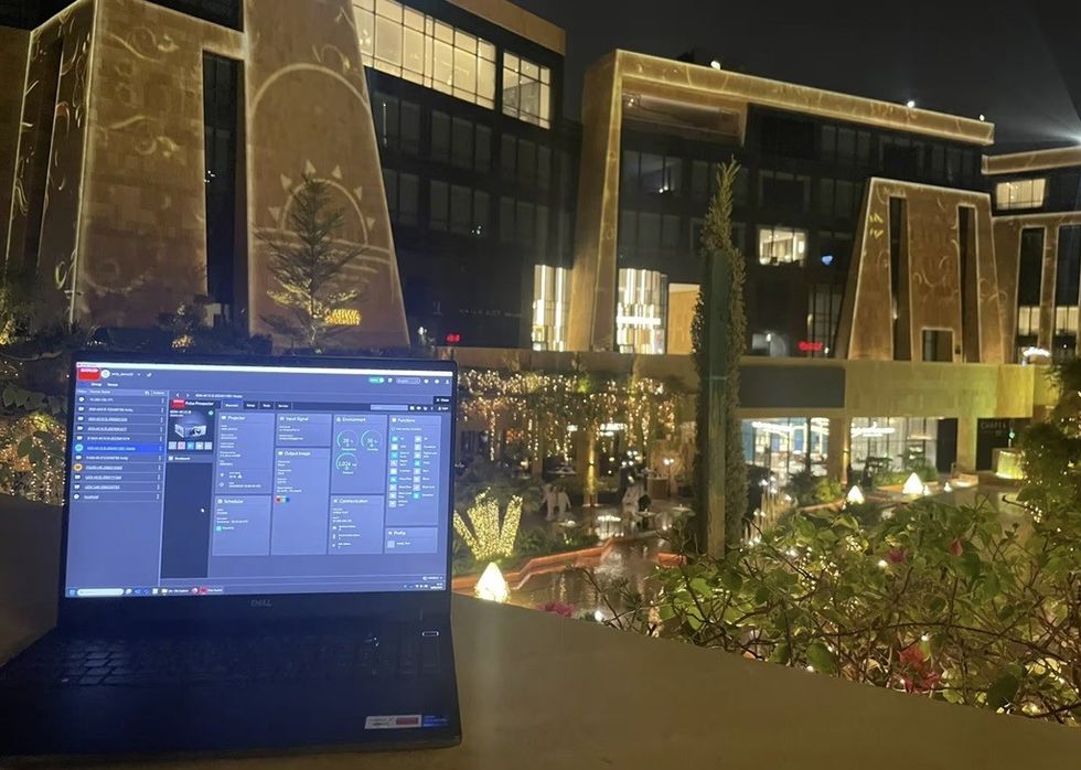 Laptop displaying software, with illuminated buildings at Via Riyadh in the background at night.