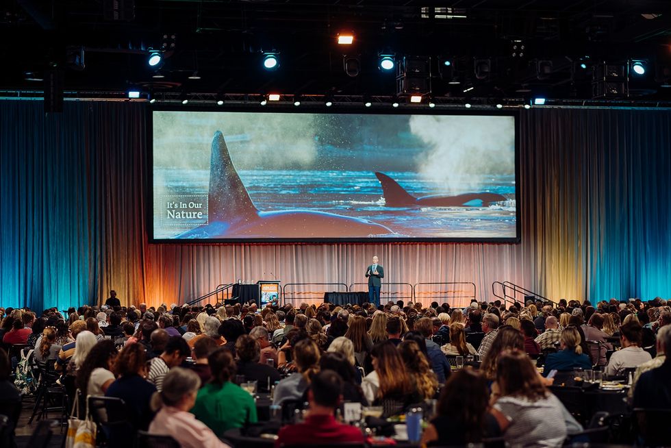 Large audience at a conference with whale image on screen.