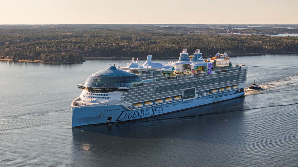 Large cruise ship called Legend of the Seas sailing on a calm river surrounded by forest.