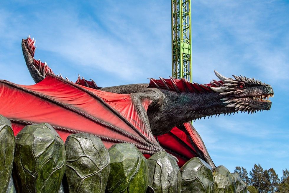 Large dragon sculpture with red wings and sharp teeth against a blue sky backdrop.
