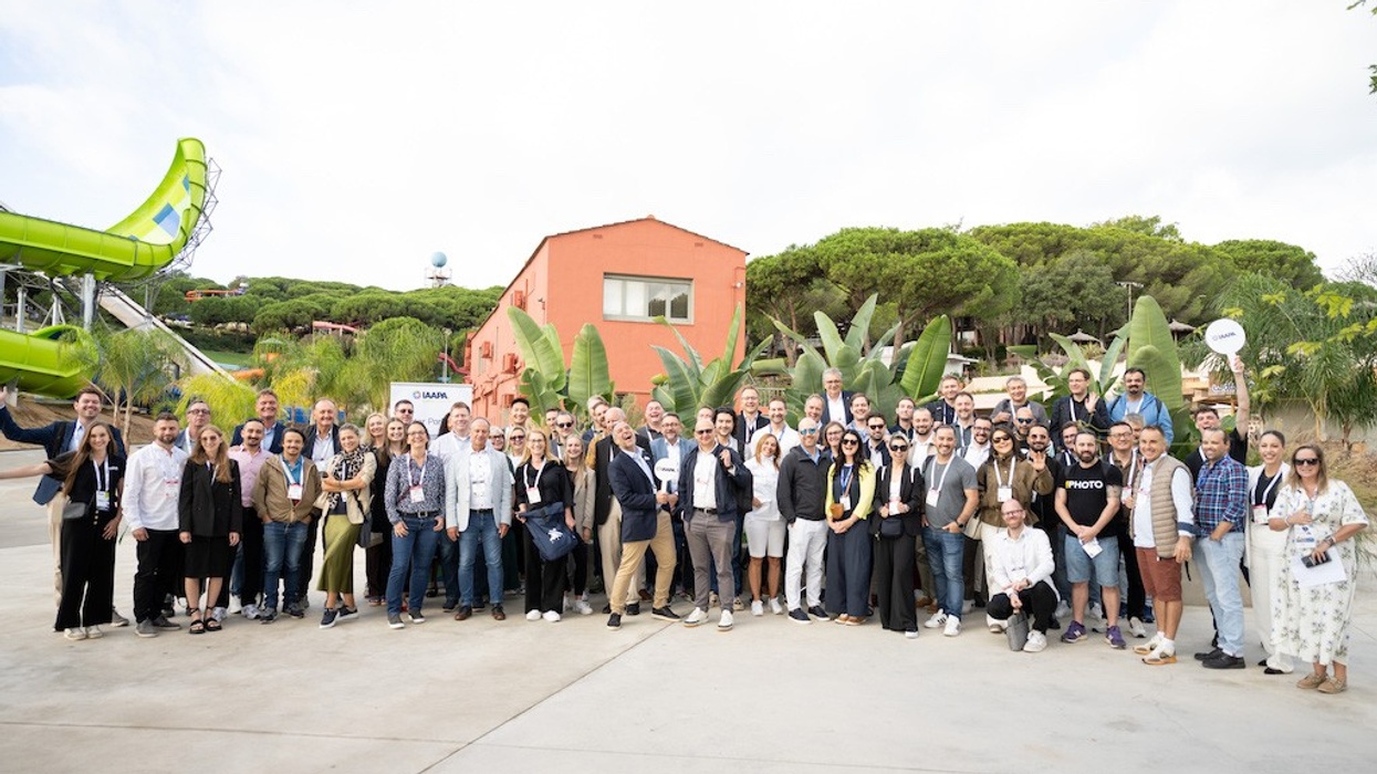Large group posing outside near a red building and green slide in a tropical setting.
