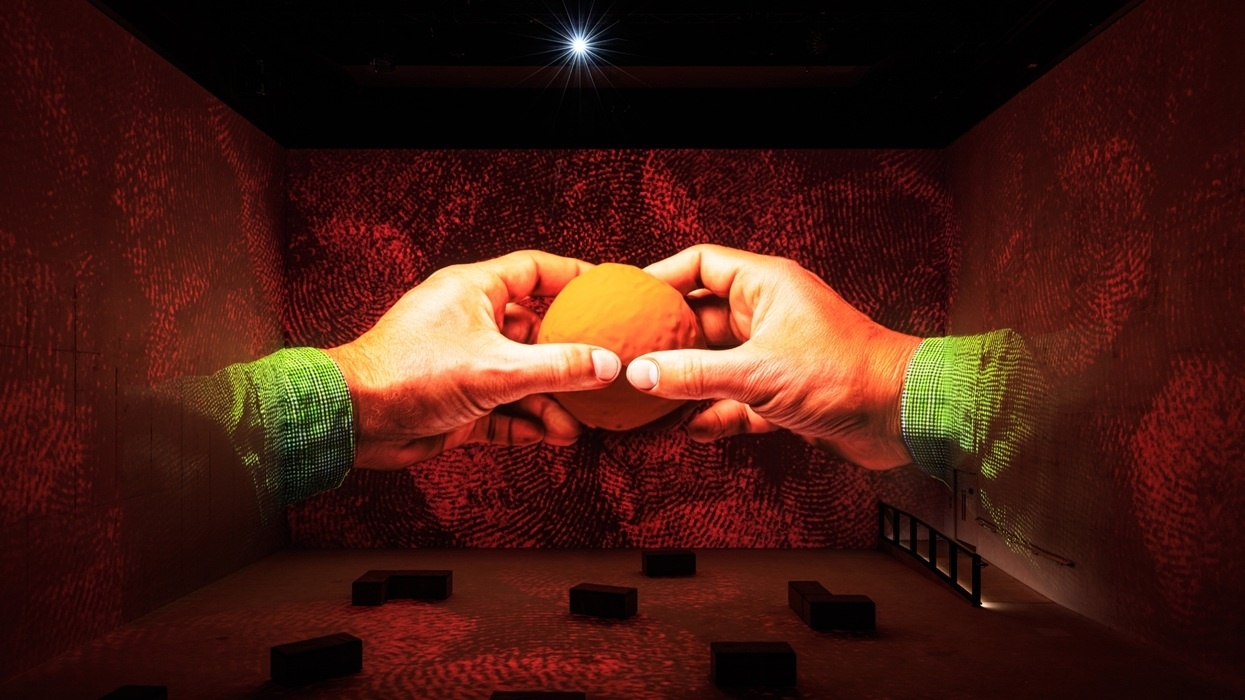 Large hands holding an orange ball, projected on red-patterned walls in Larger Than Life: Starring Wallace & Gromit, Shaun and More at Lightroom London.