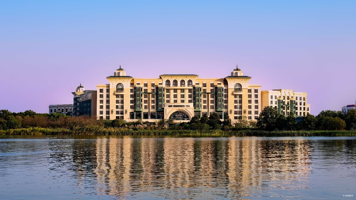 Large ornate Shanghai Disney Enchanted Star Hotel reflected in calm water beneath a pastel blue and pink sky.