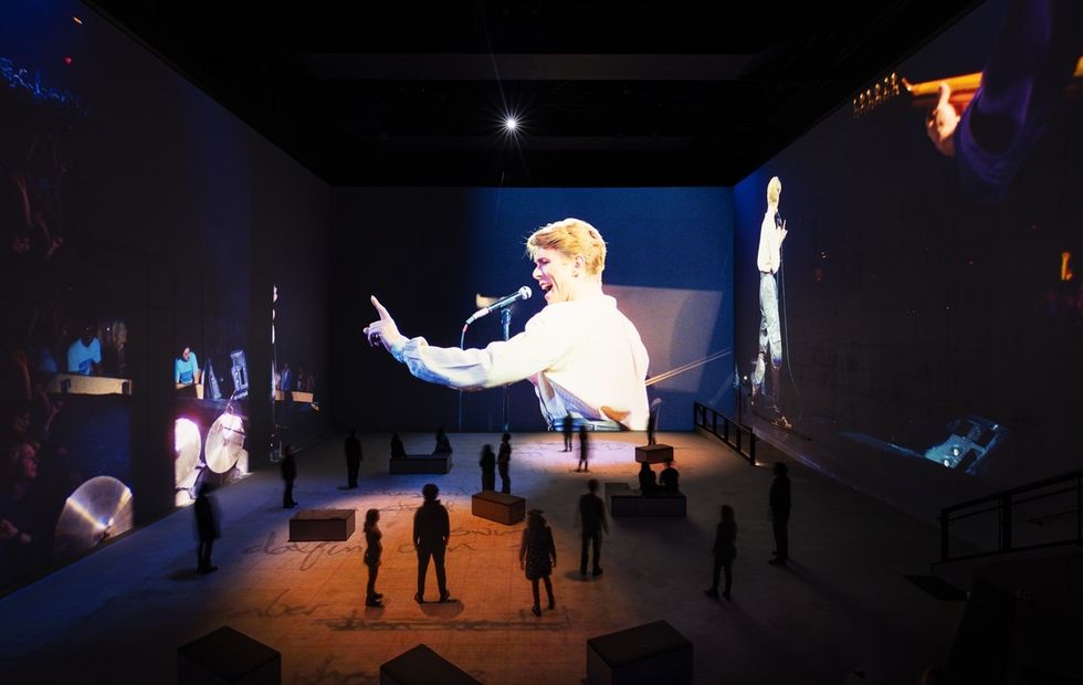 Large-scale concert projection in a dimly lit room with people observing.