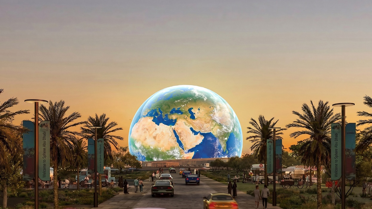 Large spherical Earth display on Sphere Abu Dhabi at sunset, flanked by palm trees and cars.