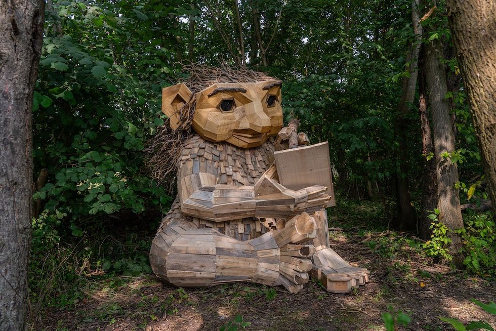 Large wood troll sculpture reading a book in a forest.