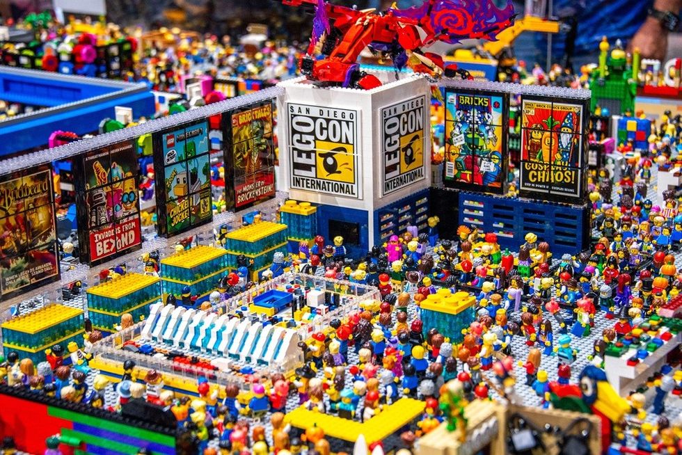 LEGO diorama depicting a crowded convention scene with a dragon model on a building.
