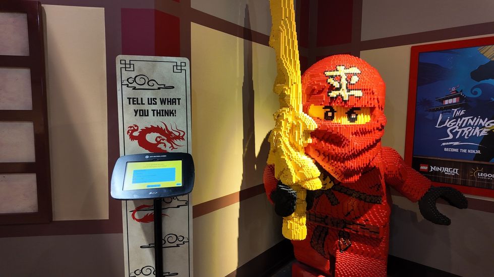 LEGO ninja model with gold sword, interactive kiosk, and "The Lightning Strike" poster.