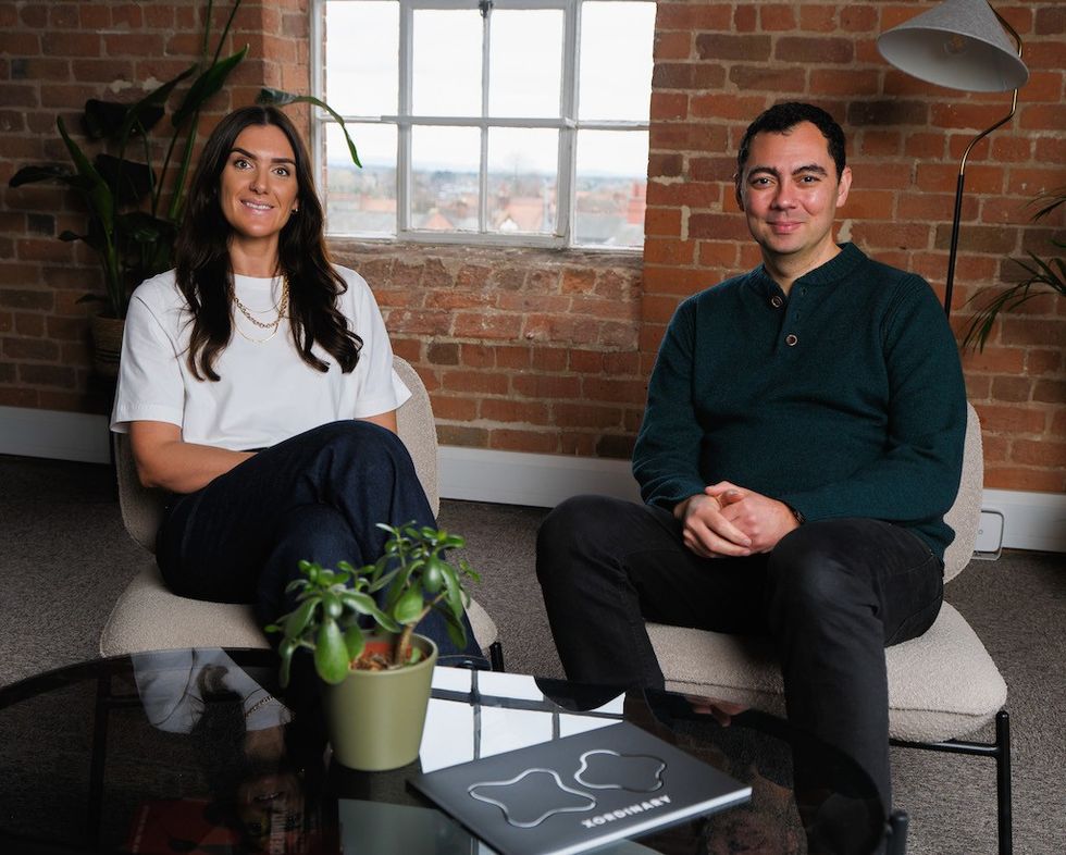 Lorna Jones and Mark Rivkin of XOrdinary sitting on chairs in a brick-walled room with a plant and lamp nearby
