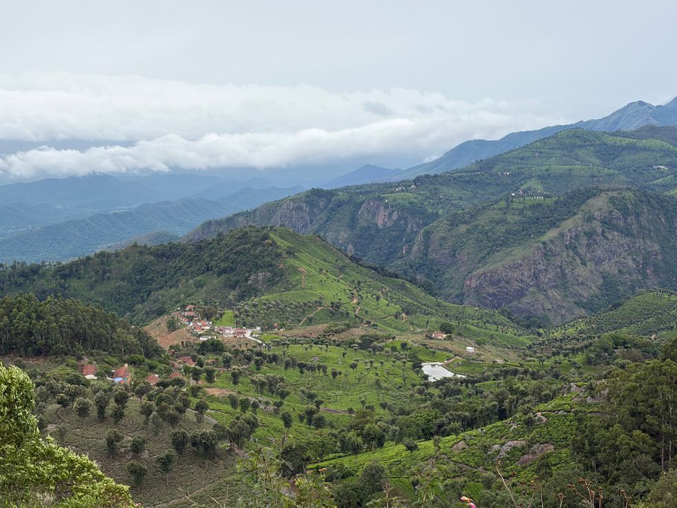 Lush green hills with scattered buildings under a cloudy sky.