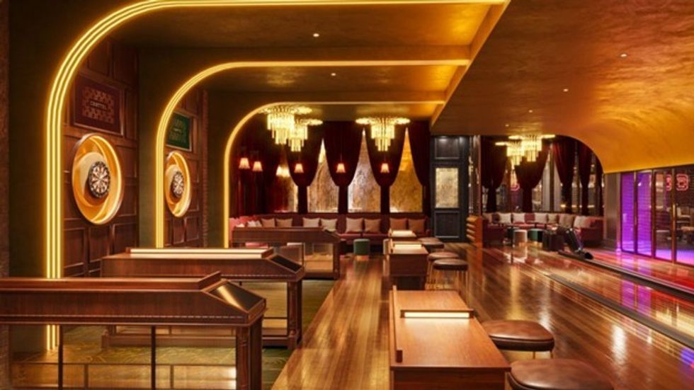 Luxurious bowling alley with chandeliers, dartboards, and wooden lanes, in dim lighting.
