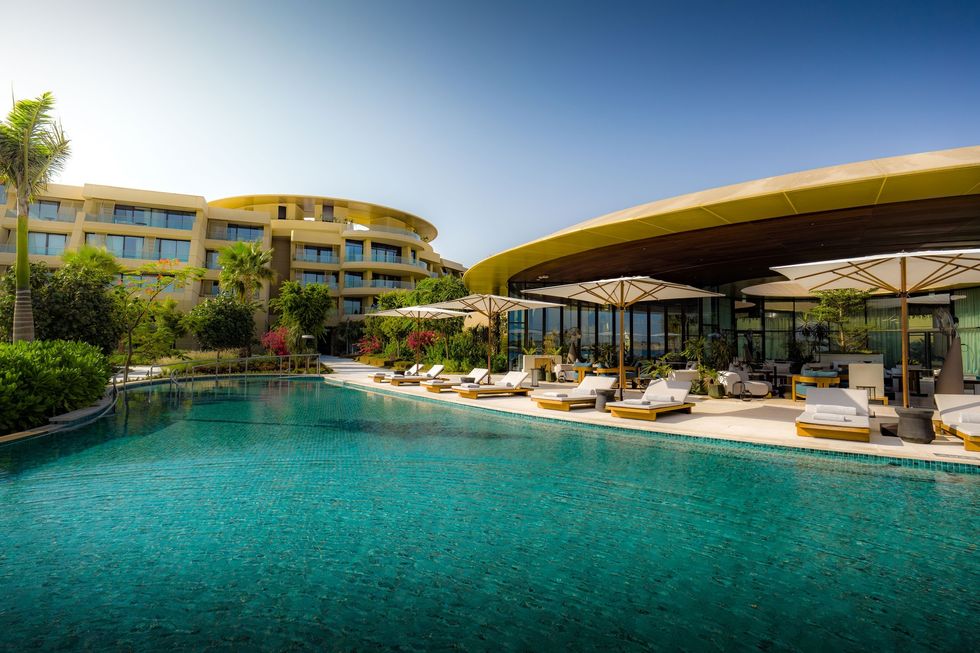 Luxurious hotel pool with sun loungers and umbrellas under a clear blue sky at Equinox Resort Amaala