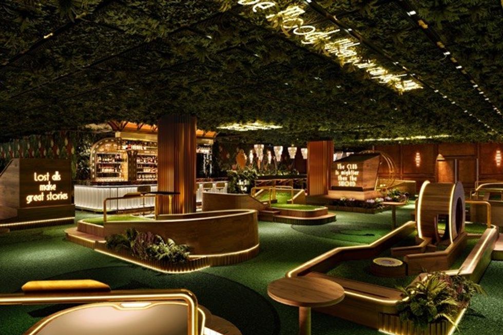 Luxurious indoor mini-golf course with lush greenery and neon signs.