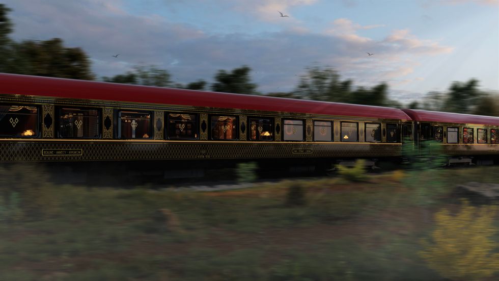 Luxurious train with red roof moving through scenic countryside at sunset.