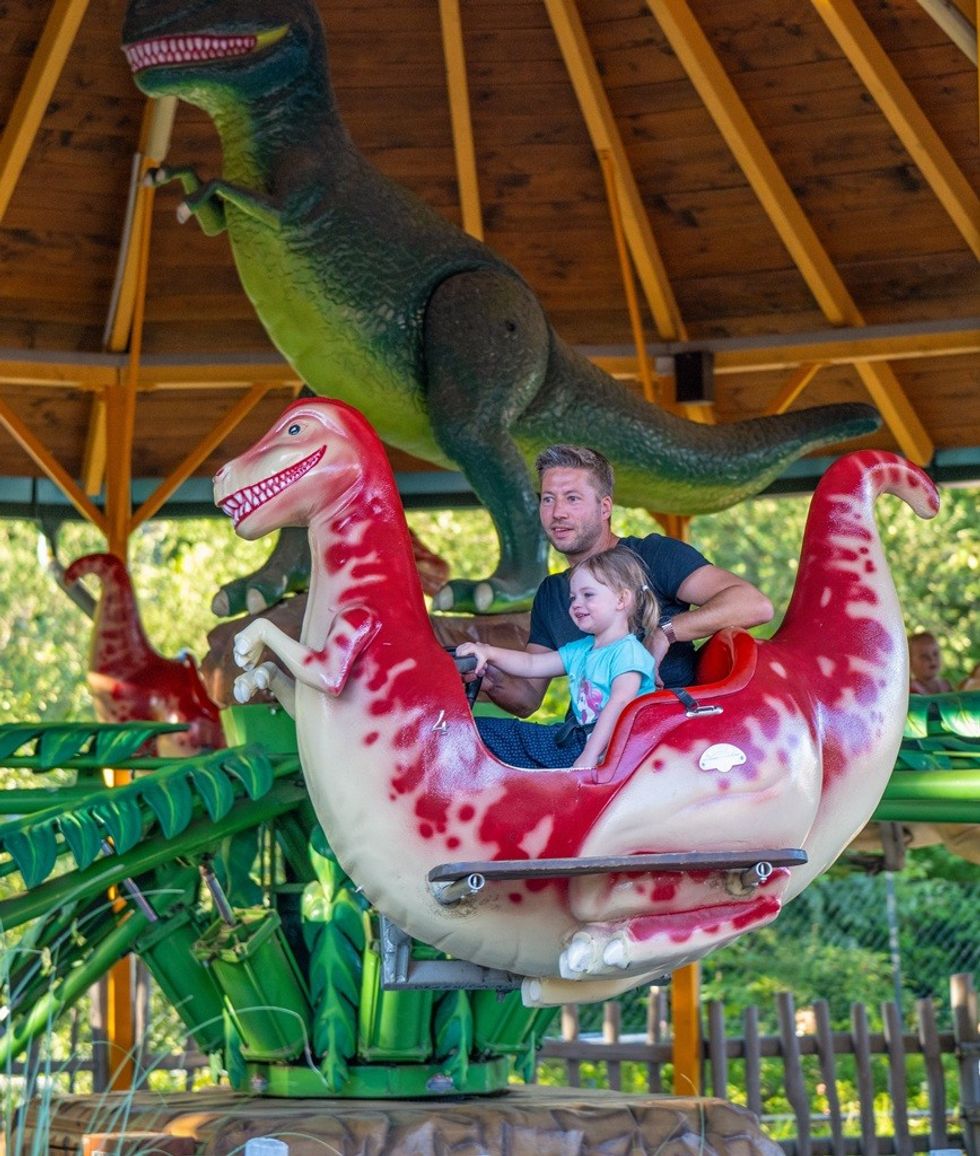 Man and child on a dinosaur-themed amusement park ride.