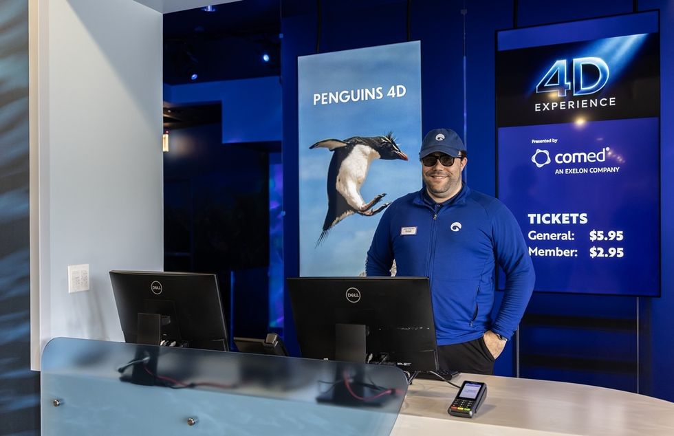 Man at a 4D experience counter with penguin poster and ticket prices displayed.