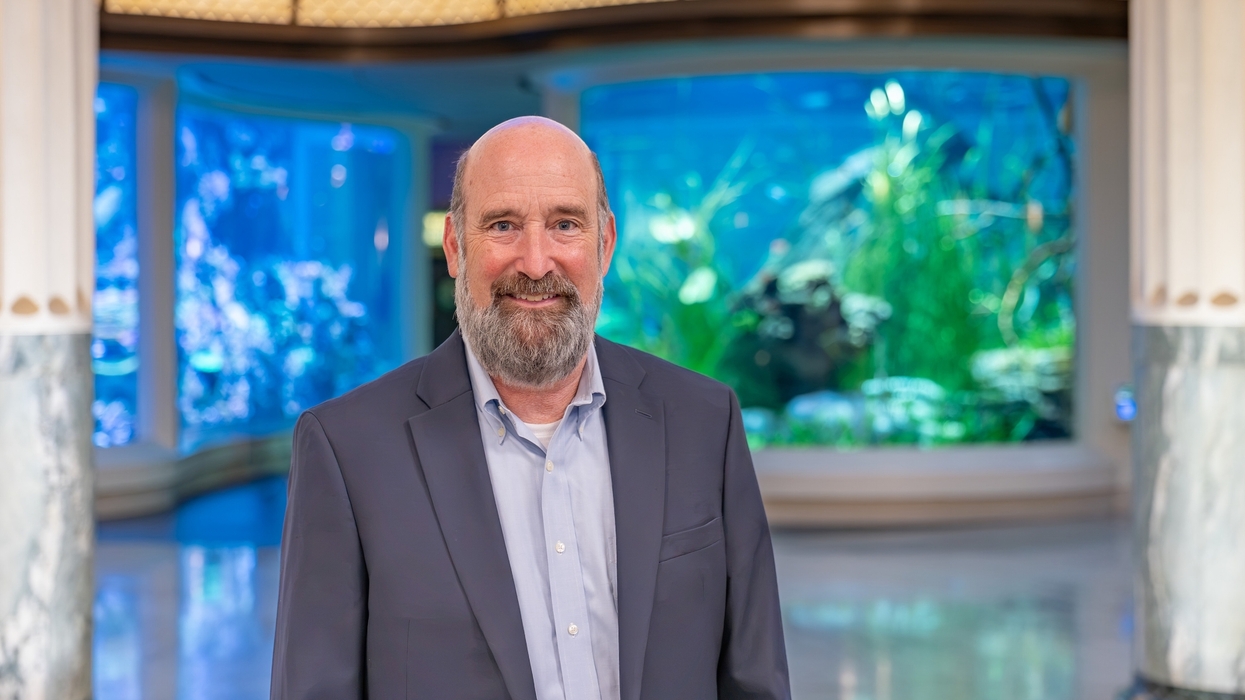 Man called Brad Rutherford in suit smiling indoors with large aquarium in the background.