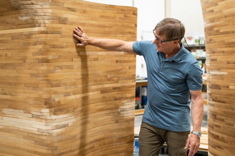 Man examining large, curved wooden structure indoors.