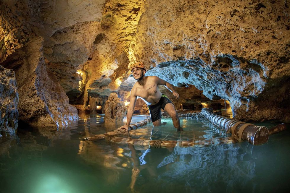 Man exploring a lit cave on a raft in shallow water.