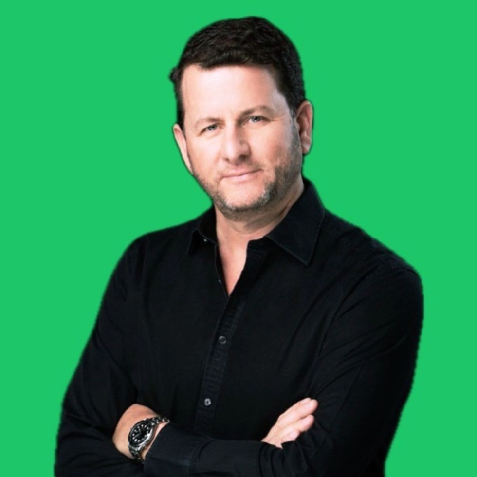 Man in a black shirt with arms crossed, standing against a green background.
