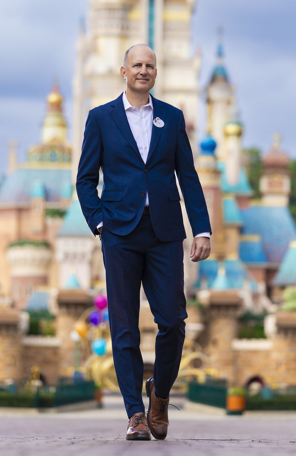 Man in a blue suit, Tim Sypko, walking in front of a colourful Disney castle at Hong Kong Disneyland