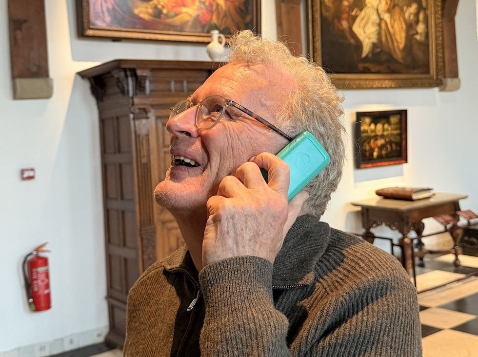 Man in a museum holds turquoise Guide-ID audio guide to ear, smiling upwards.