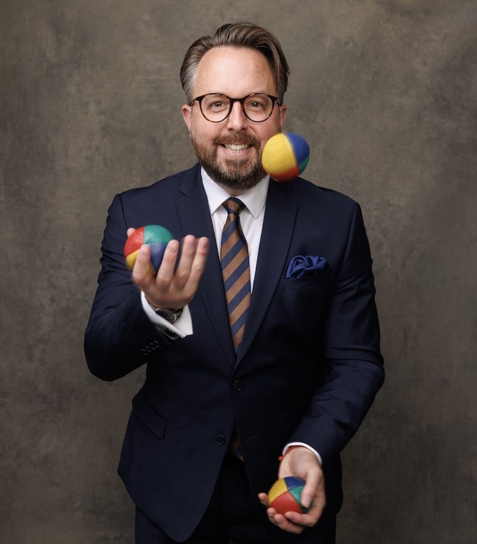 Man in a suit juggling colorful balls, smiling.