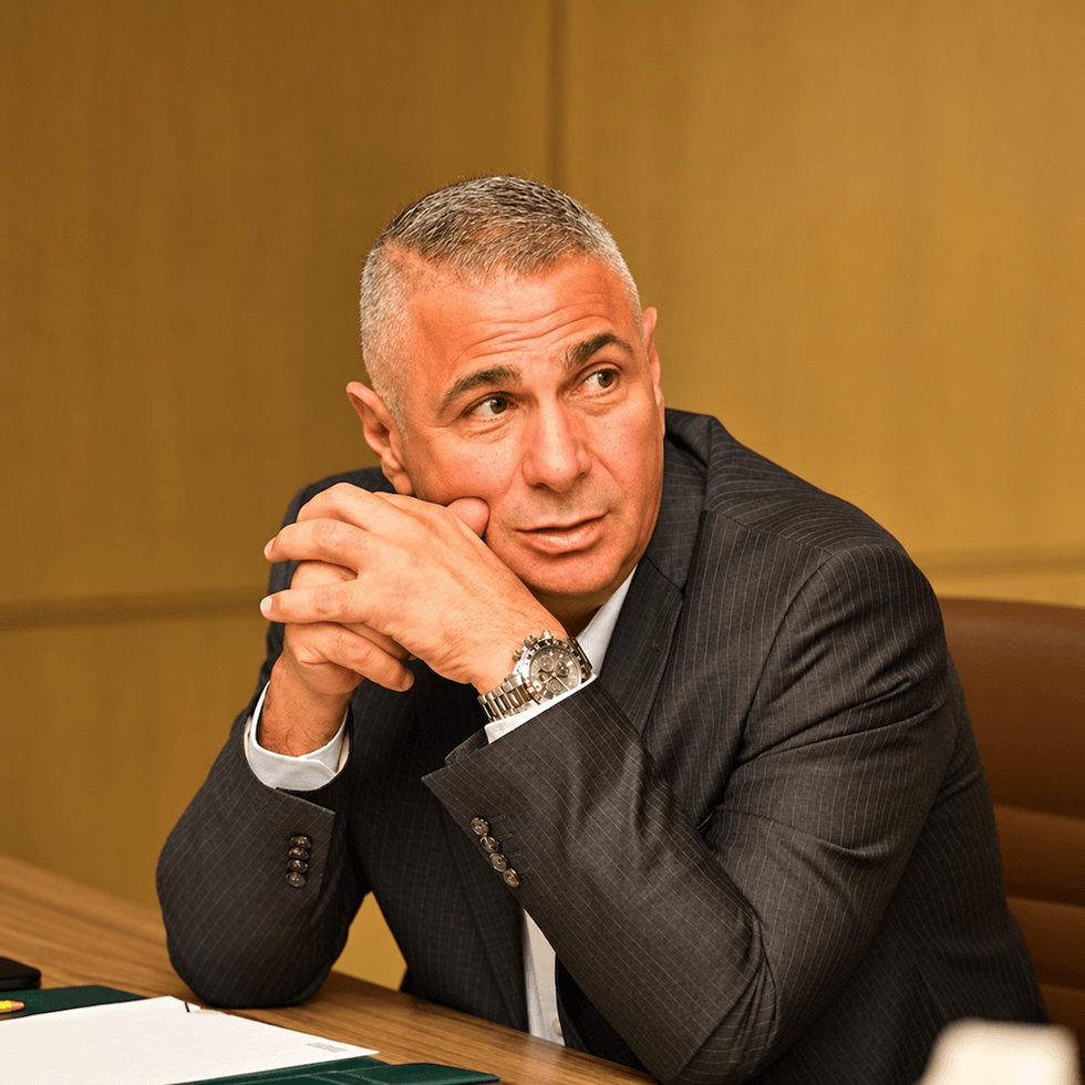 Man in a suit sitting at a table, hands clasped, looking to the side - Sarkis Kahwajian, associate VP at dmg events