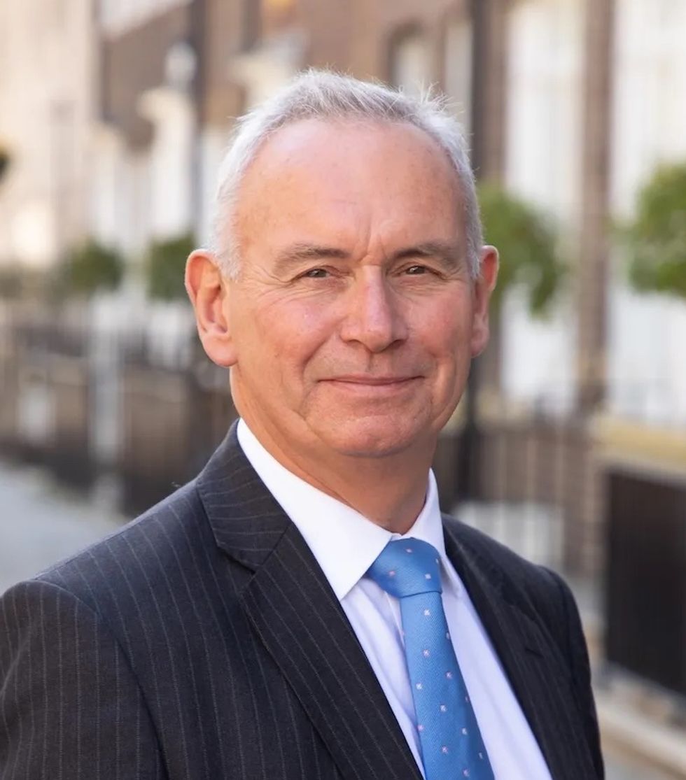 Man in a suit with a blue tie, standing outdoors.