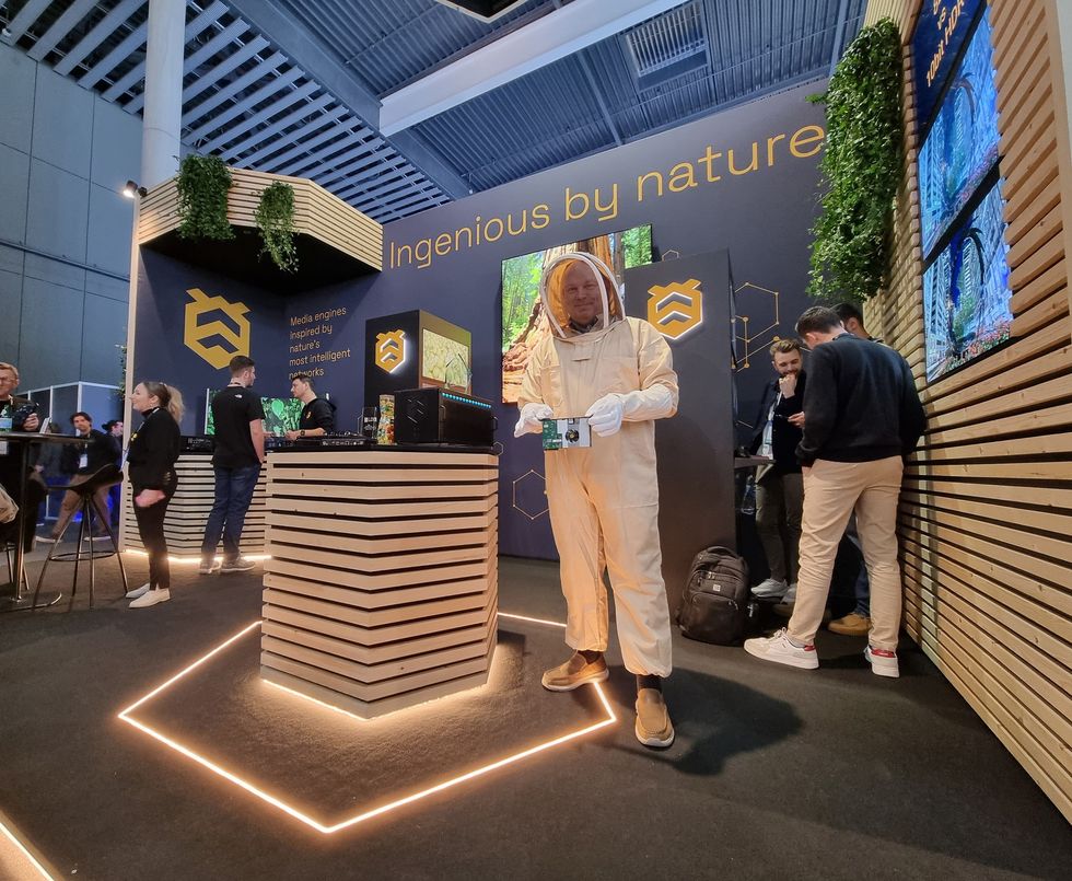 Man in beekeeper suit at tech booth with nature-inspired theme.