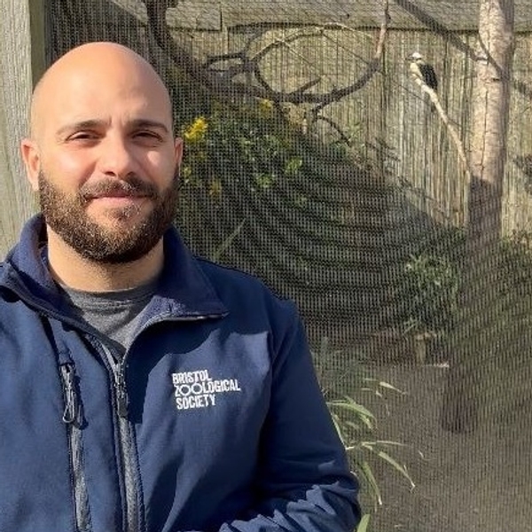 Man in blue jacket at Bristol Zoo with bird enclosure in background.
