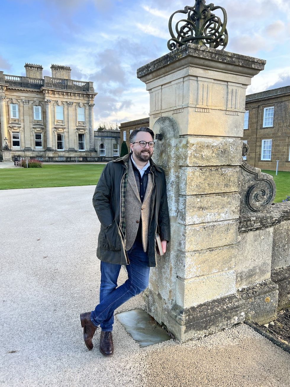 Man in casual attire leaning on a stone pillar in front of a historic building.