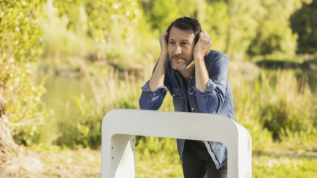 Man in denim jacket leaning on white Losonnante device in a lush, green park setting.