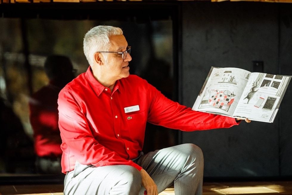 Man in red shirt, Julio Badin, holding and showing an open book with illustrations.