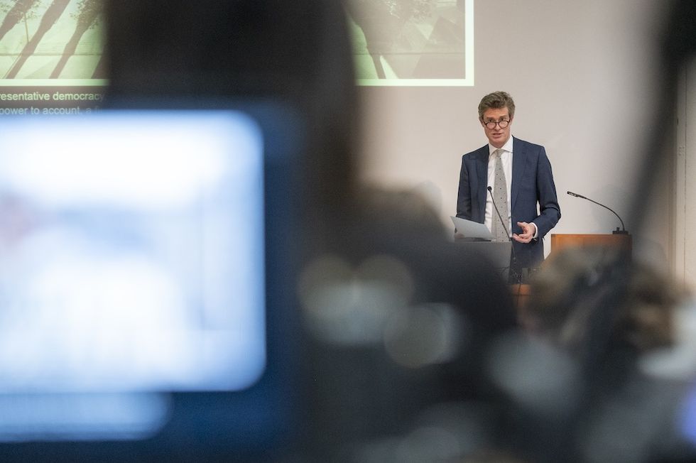 Man in suit giving a presentation, viewed through camera equipment.