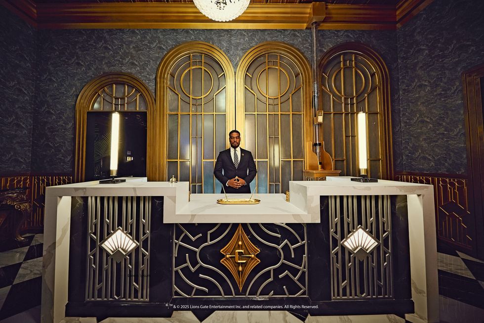 Man in suit stands behind elegant reception desk with art deco design and golden accents.