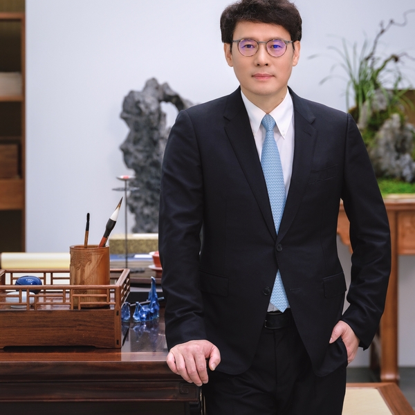 Man in suit with glasses standing by a desk with art supplies.