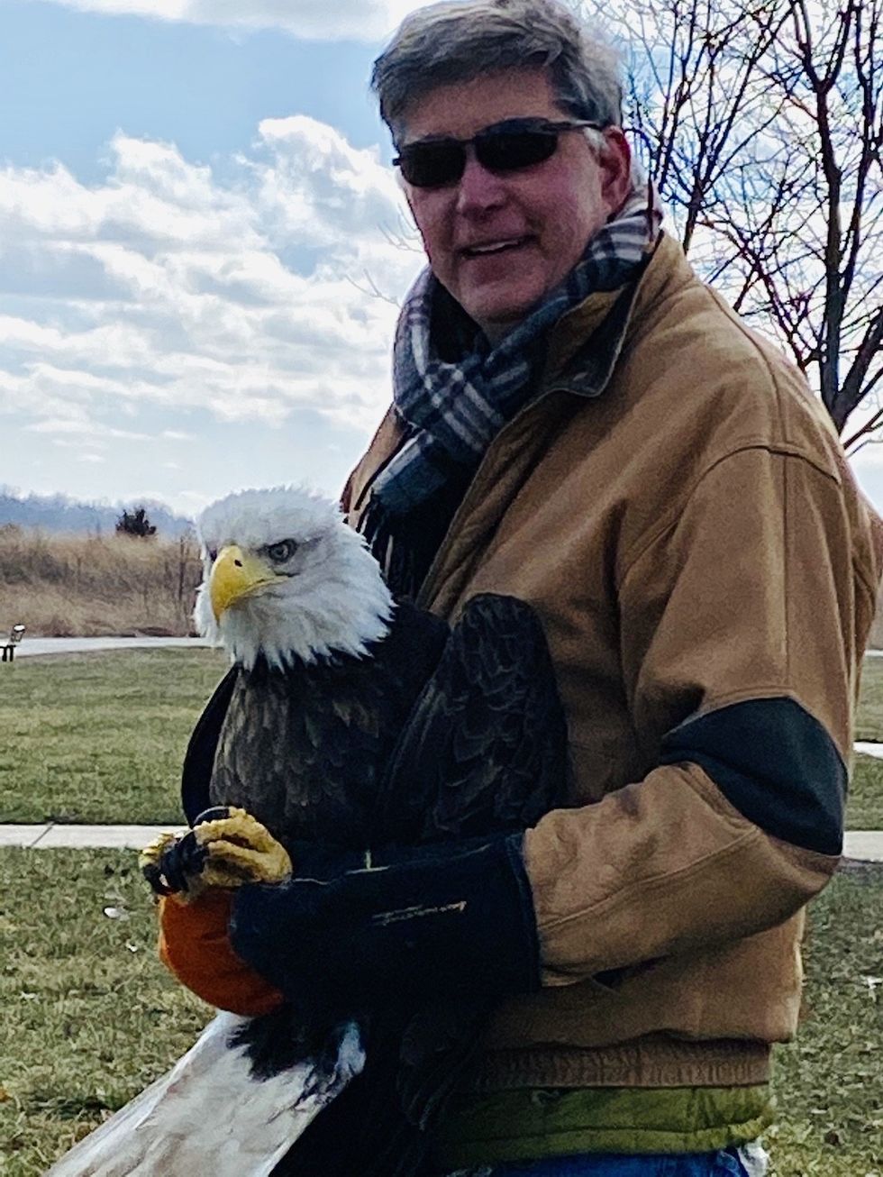 Man in sunglasses holding a bald eagle outdoors on a winter day.